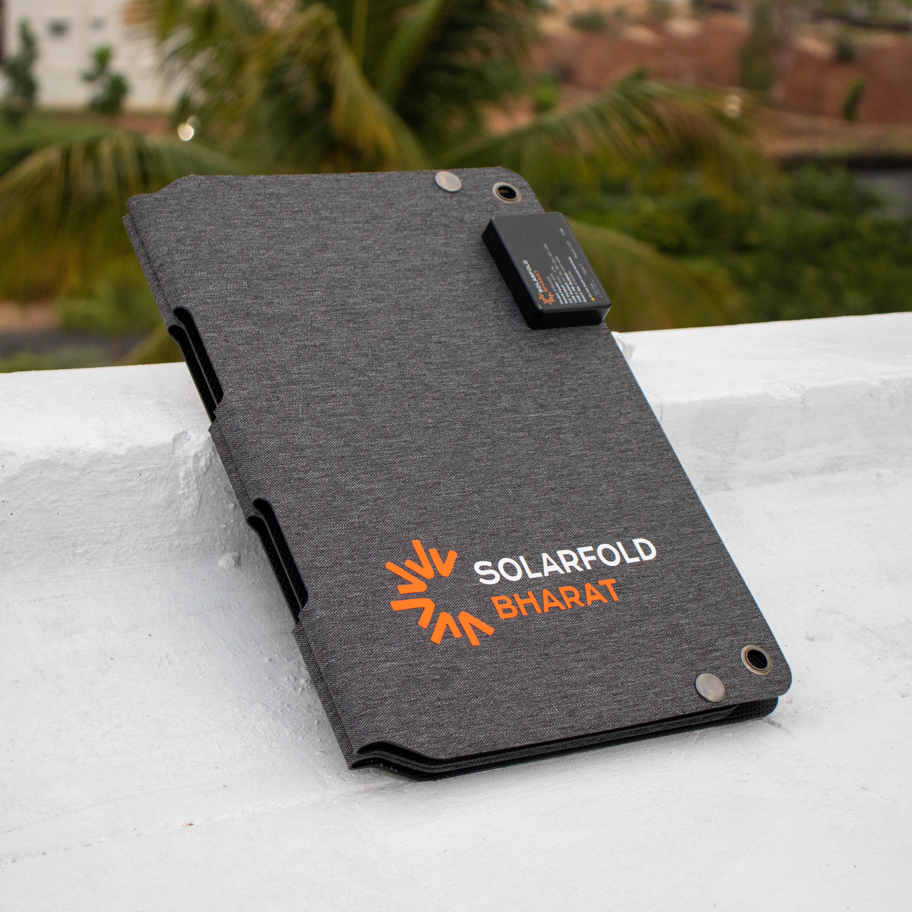Gray solar panel case with 'Solarfold Bharat' branding on a white surface with greenery in the background